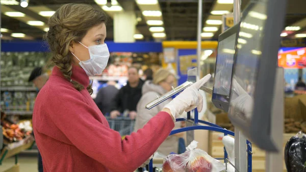 Женщина в перчатках и маске весит яблоки сенсорный экран электронные весы в супермаркете, коронавирус в общественном месте — стоковое фото