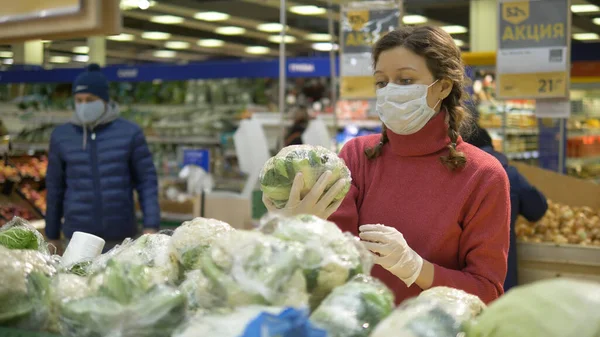 Жінка в масці і рукавичках вибирає свіжу цвітну капусту в супермаркеті, карантинний коронавірус ковід-19 — стокове фото