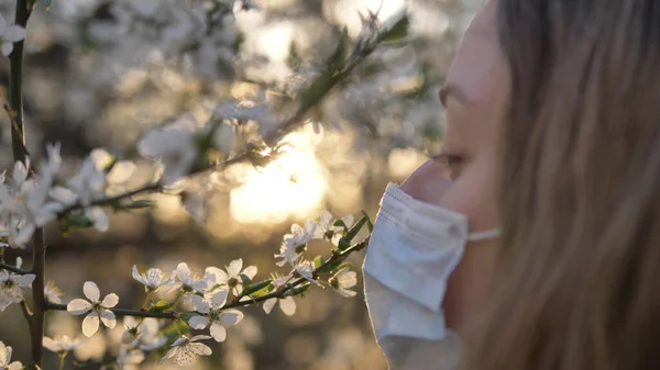 Дівчина видаляє медичну маску і снайпери, що цвітуть дерево яблуні або вишні на заході сонця крупним планом — стокове фото