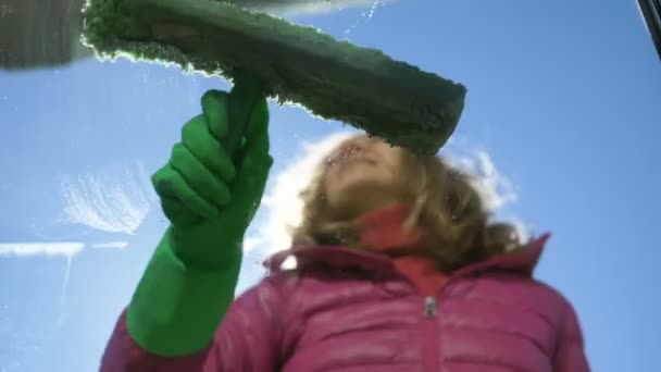 Mujer sonriente con chaqueta y guantes de goma lava la ventana sucia afuera — Vídeos de Stock