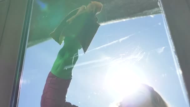 Mooi jong meisje veegt vlekken op het raam met een doek in rubber handschoenen — Stockvideo