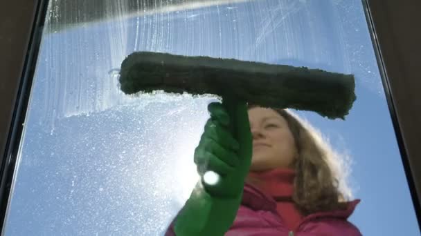 Bella ragazza lava una finestra sul balcone mette detergente con su vetro — Video Stock