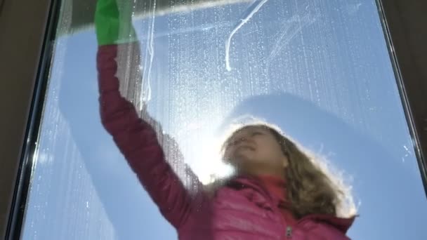 Flicka tvättar smutsiga fönster på balkong utanför med en gummipinne på en solig kall dag — Stockvideo