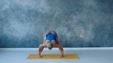 Yoga eğitmeni, stüdyoda arka bacakları esneterek omuz genişliğini mindere doğru eğiyor.