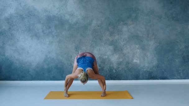 Yoga eğitmeni, stüdyoda arka bacakları esneterek omuz genişliğini mindere doğru eğiyor. — Stok video