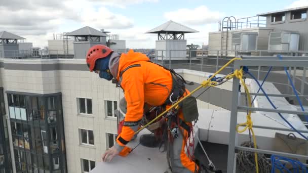 Escalador industrial en traje comprueba y fija el seguro de cuerda en el techo del edificio antes del descenso — Vídeo de stock