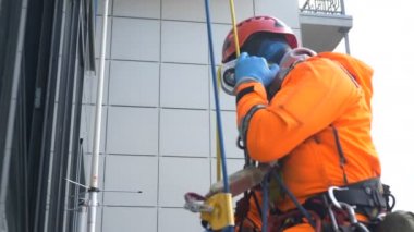 Kauçuk eldivenli endüstriyel tırmanıcı, yüksek bir binanın dışındaki iniş aletini kullanarak ipten aşağı kayıyor.