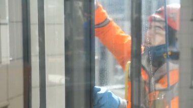 Endüstriyel tırmanışçılar camları tulumla, kaskla ve eldivenlerle yavaş çekimde temizler.