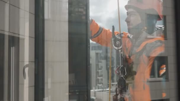 Glimlachende industriële klimmer wast ramen op grote hoogte buiten tegen achtergrond zonlicht — Stockvideo