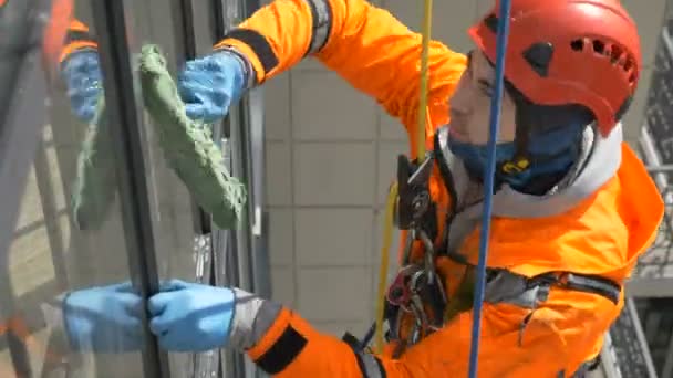 Industriële klimmer in rubber handschoenen harde hoed en pak wast raam buiten gebouw — Stockvideo