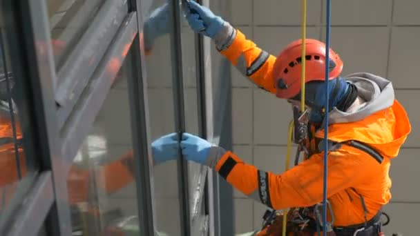 Industriële klimmer in oranje overall en helm wast ramen op hoog gebouw buiten. — Stockvideo