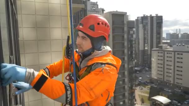 Un grimpeur professionnel en gants de caoutchouc lave les fenêtres en haute altitude — Video