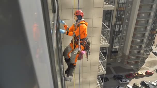 Профессионально оборудованный промышленный альпинист в шлеме и перчатках моет окна с винтом на высоком здании в современном жилом комплексе — стоковое видео