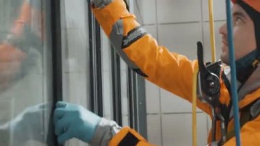 Pencere temizleme başlığı ve eldivenler apartmanın dışındaki camları plastik vidayla siliyor.