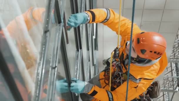 Industriële klimmer ruitenreiniger in helm en handschoenen wast ramen op hoog gebouw bovenaanzicht camera beweging — Stockvideo