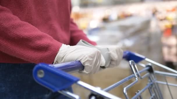 Femme dans un supermarché roule un chariot d'épicerie en gants de caoutchouc gros plan. Protège contre le coronavirus . — Video