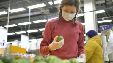 Lastik eldivenli ve tıbbi maskeli kız dikkatle limonu seçiyor, C vitaminini arttırıyor.