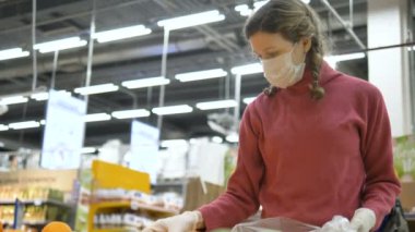 Tıbbi maskeli ve lastik eldivenli kız dikkatle portakalları seçer, C vitamini artar.