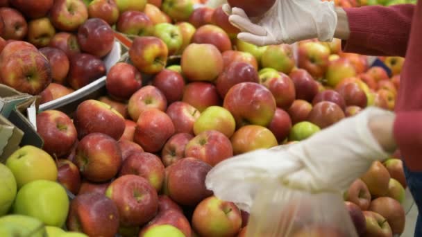 Femme en gants de caoutchouc cueille des pommes fraîches et les met dans un sac en plastique au supermarché. Protection contre le coronavirus . — Video