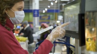 Eldivenli ve maskeli kadın, süpermarkette dokunmatik ekran elektronik terazisinde parmak basıyor, halka açık yerde koronavirüs var.