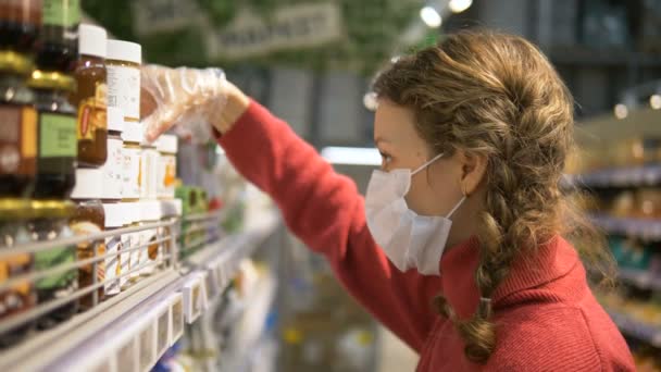 Maskeli ve eldivenli kızın portresi süpermarketteki ürünlerin etiketlerini, kişisel koruma koronavirüsünü gösteriyor. — Stok video