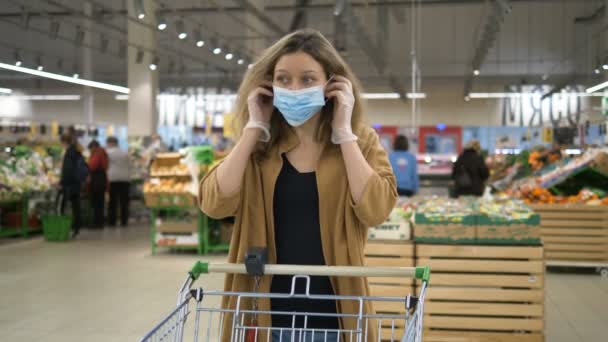 Девушка надевает медицинскую маску в супермаркете, чтобы защитить себя от пандемии коронавируса — стоковое видео
