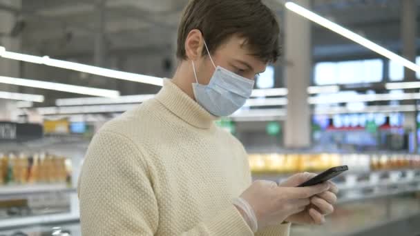 Man in a medical mask and rubber gloves stands in a supermarket with a smartphone. Protective measures against covid-19. — Stock Video