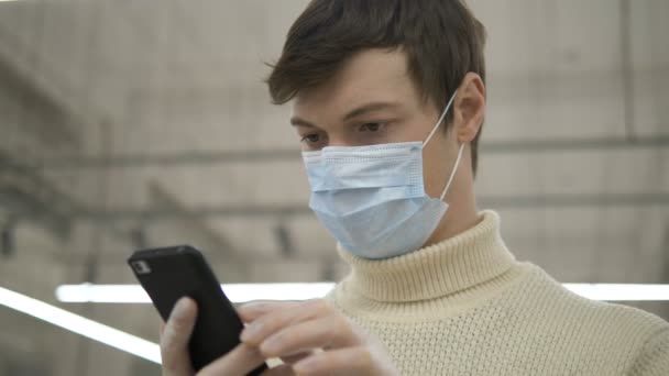 Homme en masque de protection gants en caoutchouc lecture nouvelles sur smartphone à l'intérieur — Video