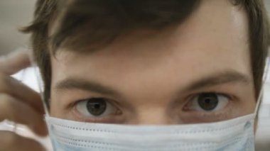 Adam tıbbi maske takıyor ve kameraya yakından bakıyor. Koronovirüse karşı koruma sağlıyor.