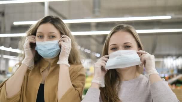Zwei Freundinnen setzen in einem Supermarkt medizinische Masken in Gummihandschuhen auf, seufzen traurig und schauen sich an. Schutzmaßnahmen gegen die Coronavirus-Pandemie. — Stockvideo