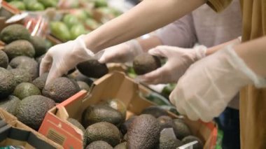 Koruyucu lastik eldivenli kızlar süpermarkette avokadoyu tercih ederler. Koronavirüs salgınından korunmak için alınan önlemler..