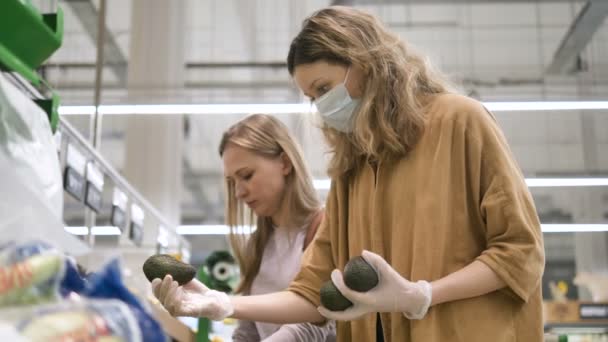 Женщины в медицинских перчатках и маске выбирают авокадо в супермаркете — стоковое видео