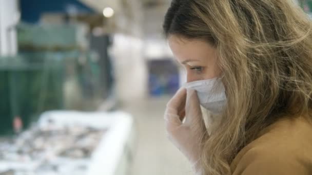 Девушка в защитной маске тщательно подбирает продукты в супермаркете, карантинные меры безопасности короновируса — стоковое видео