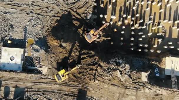 Aerial top view zoom effect excavators digging ground pit for pouring the foundation and laying concrete piles on a sunny day — Stock Video