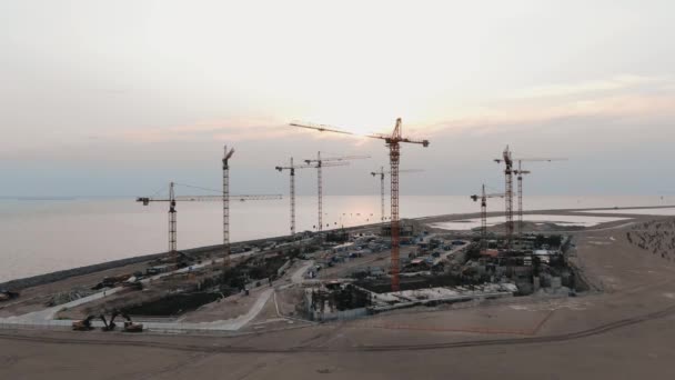 Guindastes de construção aérea ao pôr do sol em um canteiro de obras na baía — Vídeo de Stock