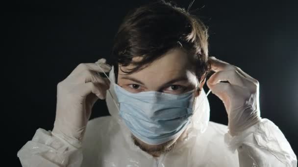 Coronavirusinfectie. jonge man zet op medisch masker en witte jumpsuit met kap — Stockvideo