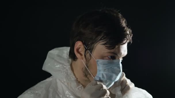 Coronavirus pandemie covid-19, man met rubberen handschoenen zet op masker in stoffige kamer op zwarte achtergrond — Stockvideo