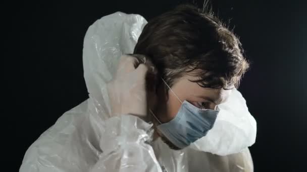 医師は、ゴム手袋、コロナウイルスのパンデミックcovid-19と黒の背景にほこりっぽい部屋に白とマスクを置きます — ストック動画