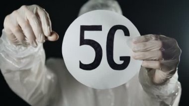 Beyaz antiviral koruyucu giysili ve lastik eldivenli adam 5G tableti tutuyor ve baş parmağını aşağı gösteriyor.