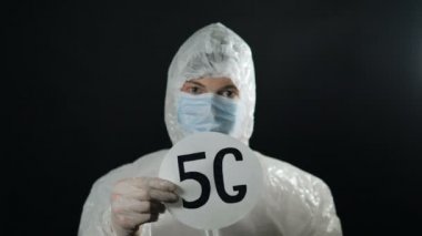 Beyaz antiviral giysili adam 5G 'yi tutuyor. Alüminyum folyo şapka takıyor.