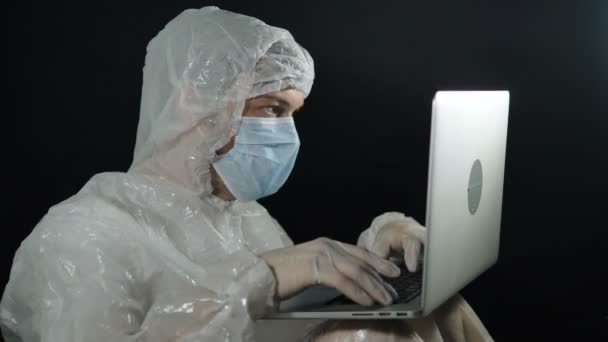 Tudós férfi védőruhában és maszkban gépel egy laptopos estén betegjelentéseket ír a laborban — Stock videók