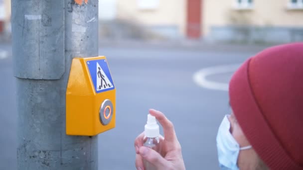 Maskeli ve eldivenli bir adam trafik lambasındaki yaya geçidi tuşuna antiseptikle basıp üzerine tıklatıyor. — Stok video