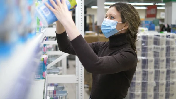 Een jonge vrouw met een medisch masker neemt veel toiletpapier mee in een supermarkt. — Stockfoto