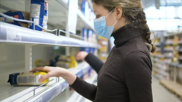 Жінка в медичній масці бере останню сумку з зернових в магазині, порожні полиці супермаркетів . — стокове фото