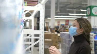 Tıbbi maskeli bir kız süpermarketten bir sürü tuvalet kağıdı paketi alır.