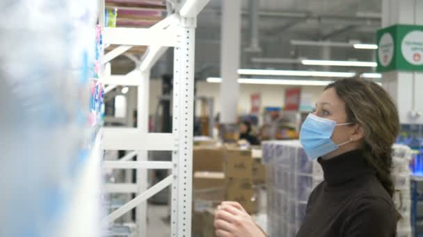 Tıbbi maskeli bir kız süpermarketten bir sürü tuvalet kağıdı paketi alır. — Stok video