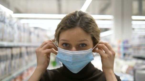 Chica se pone una máscara de protección médica y da pulgares en el supermercado — Vídeos de Stock