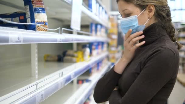 Panic coronovirus. sad woman in mask stand at empty shelf in supermarket — Stock Video