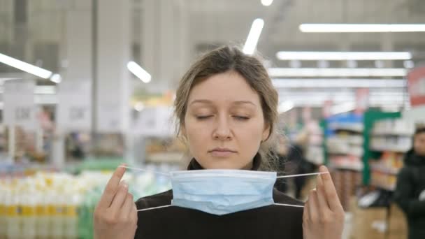 A young woman puts on a medical mask in a grocery supermarket close up — Stock Video