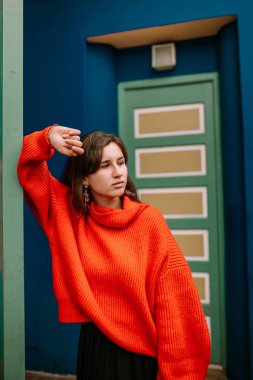 Genç kadın bir sütunda renkli bir evde kırmızı kazak ile eğilerek